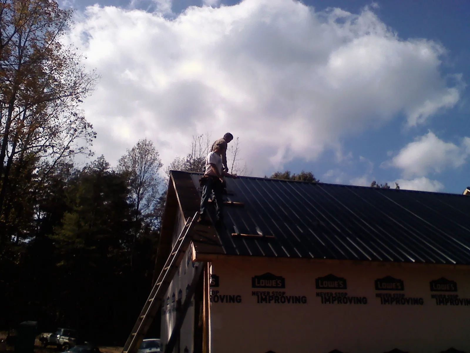 Roofer fastening dark metal panels high against a cloudy sky, from a Roof Inspection job in Irvington